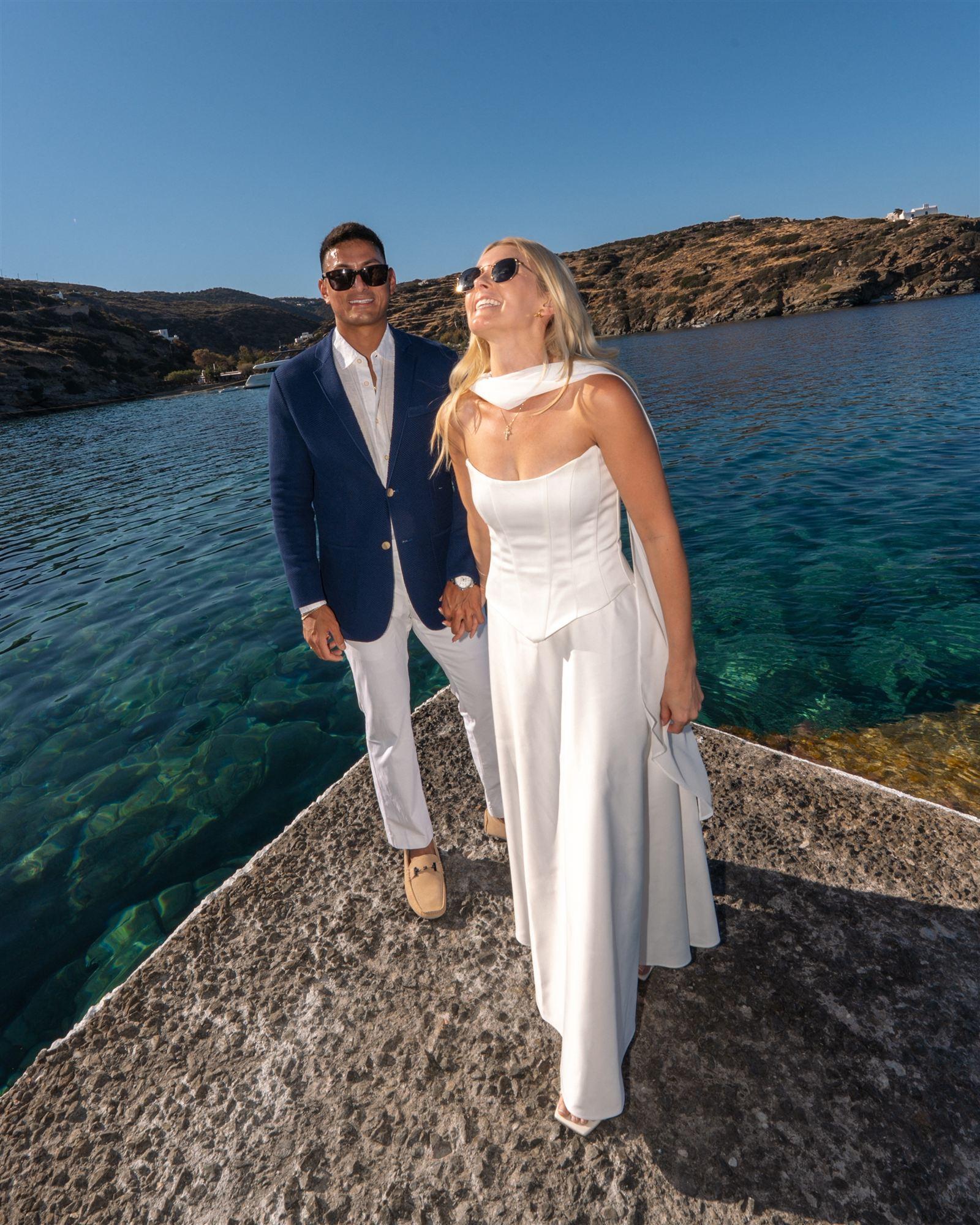 Couple standing together at the edge of a stone pier over turquoise water