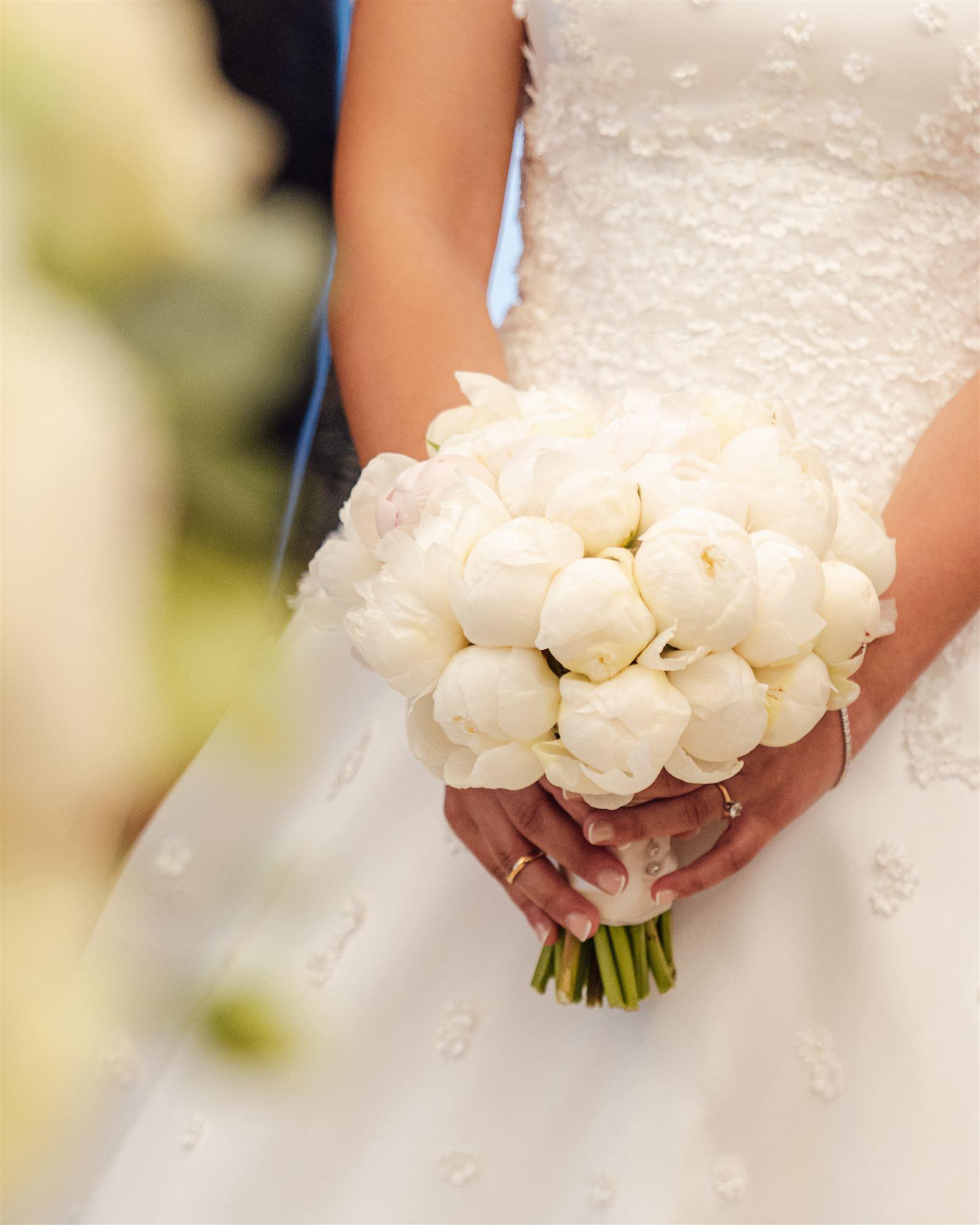 Close detail of a white bouquet held against a wedding dress before the ceremony