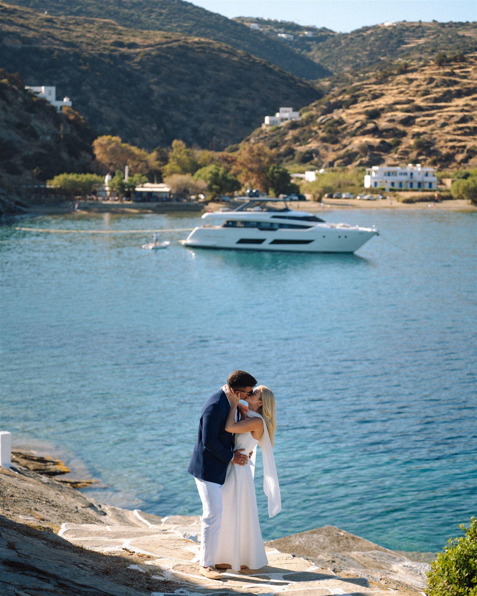Couple embracing on a white cliff edge above a turquoise bay, boat in the distance
