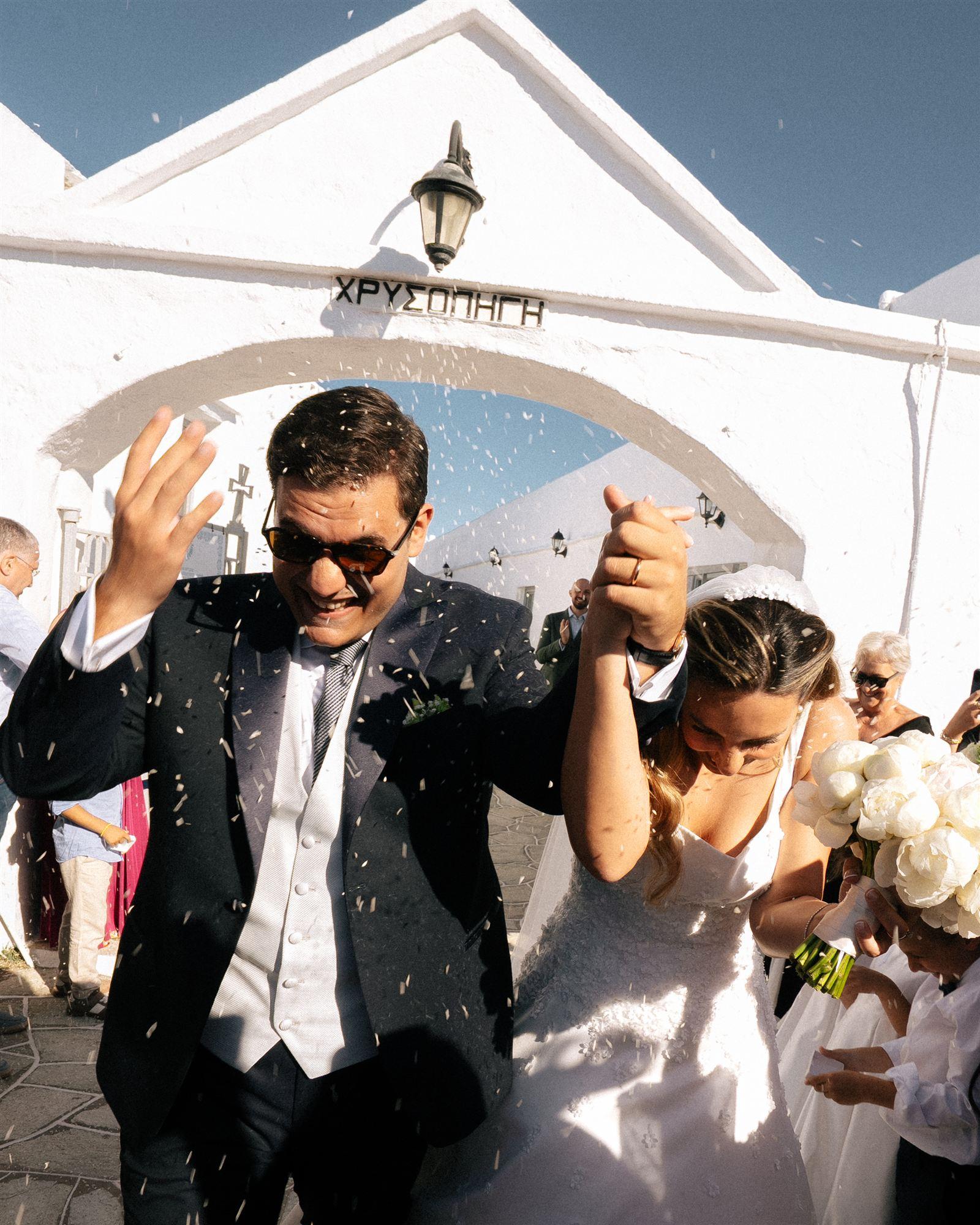 Bride and groom celebrating outside a whitewashed chapel as guests throw confetti