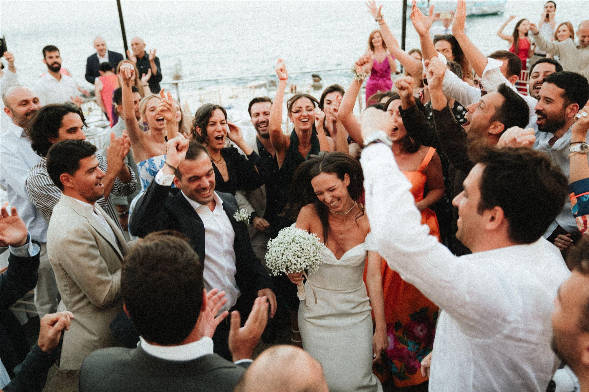 A large group of guests with arms raised, cheering for the couple at the reception