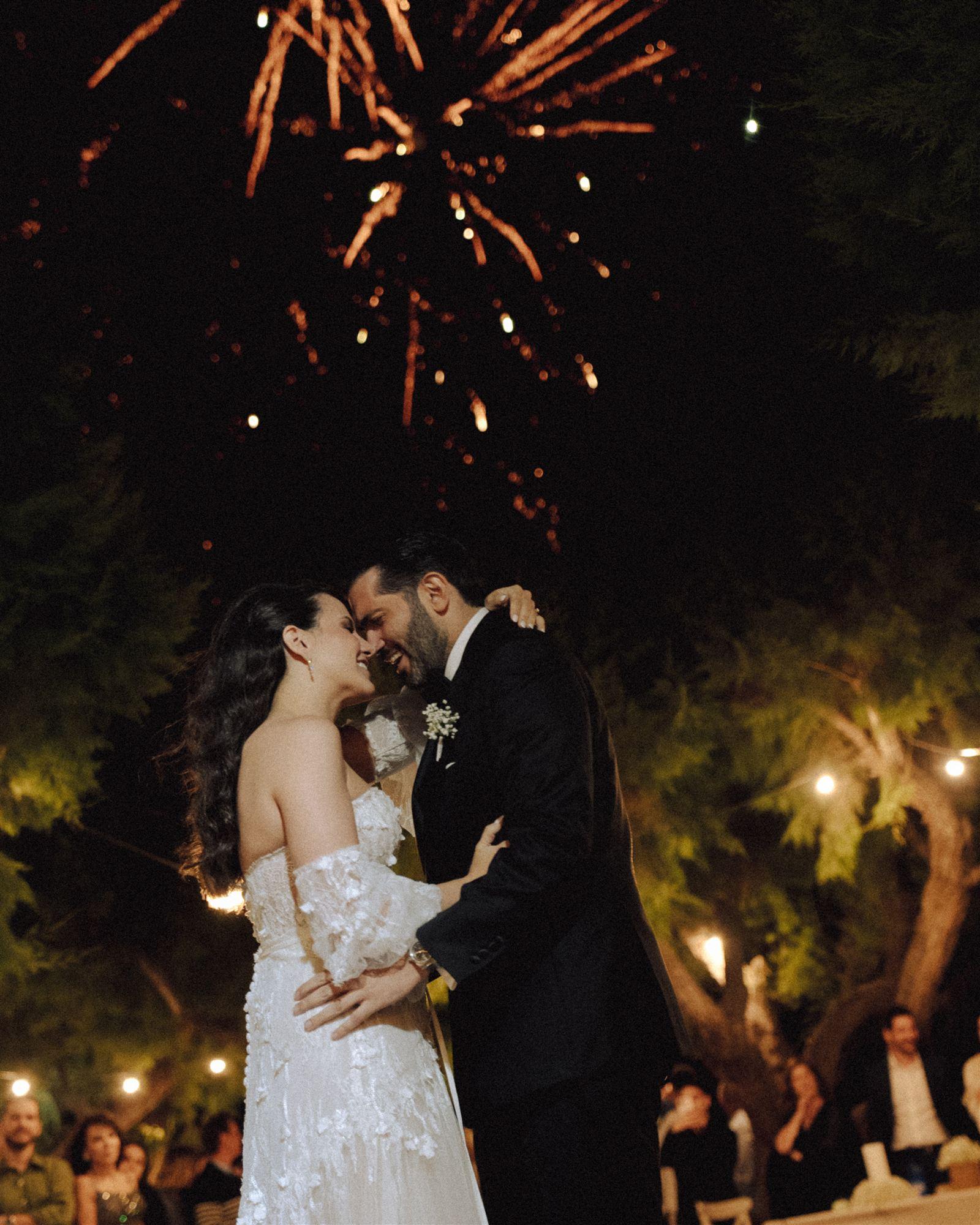 Bride and groom embracing during their first dance as fireworks light up the night sky