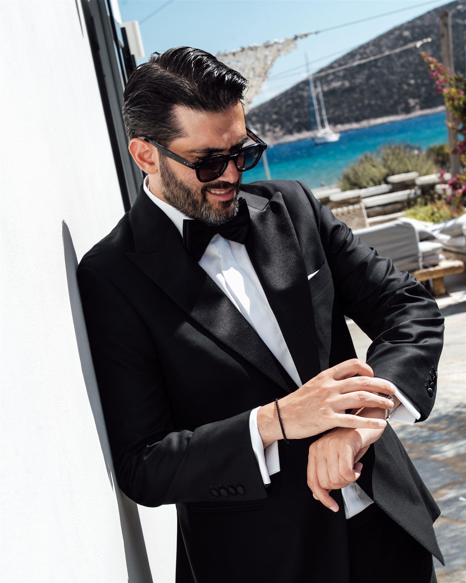 Groom checking his watch while getting ready, sea visible in the background