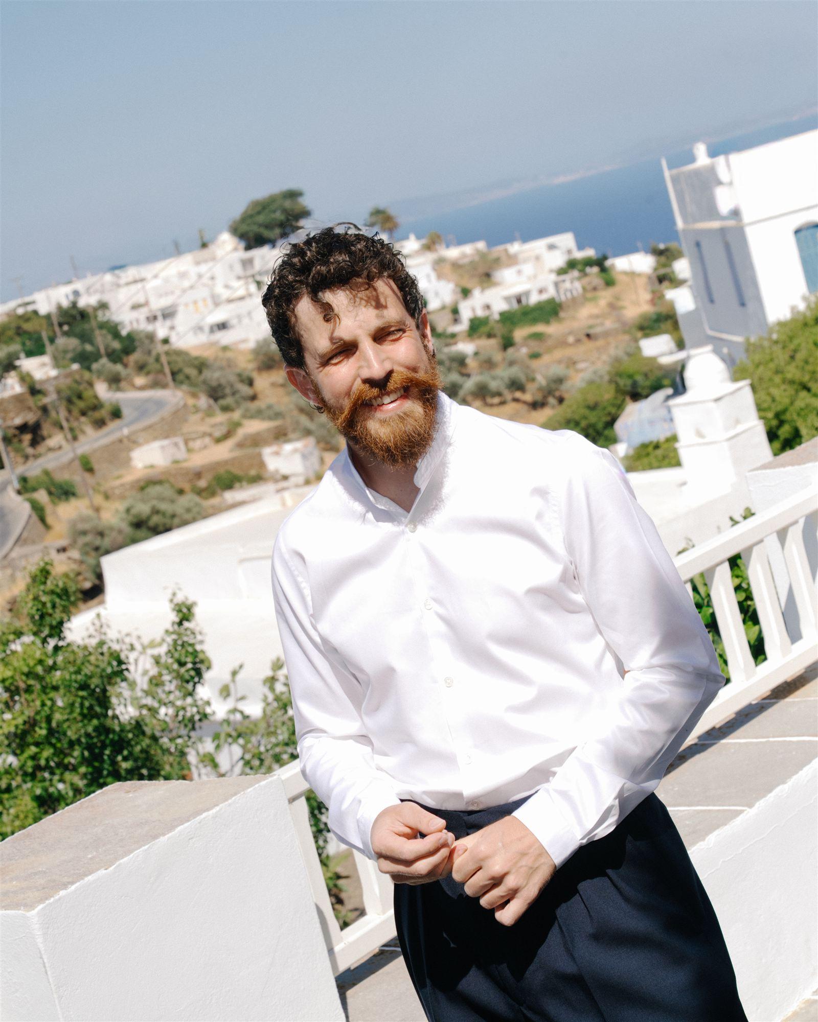 Groom in a white shirt, sleeves rolled up, caught mid laugh in the morning sun