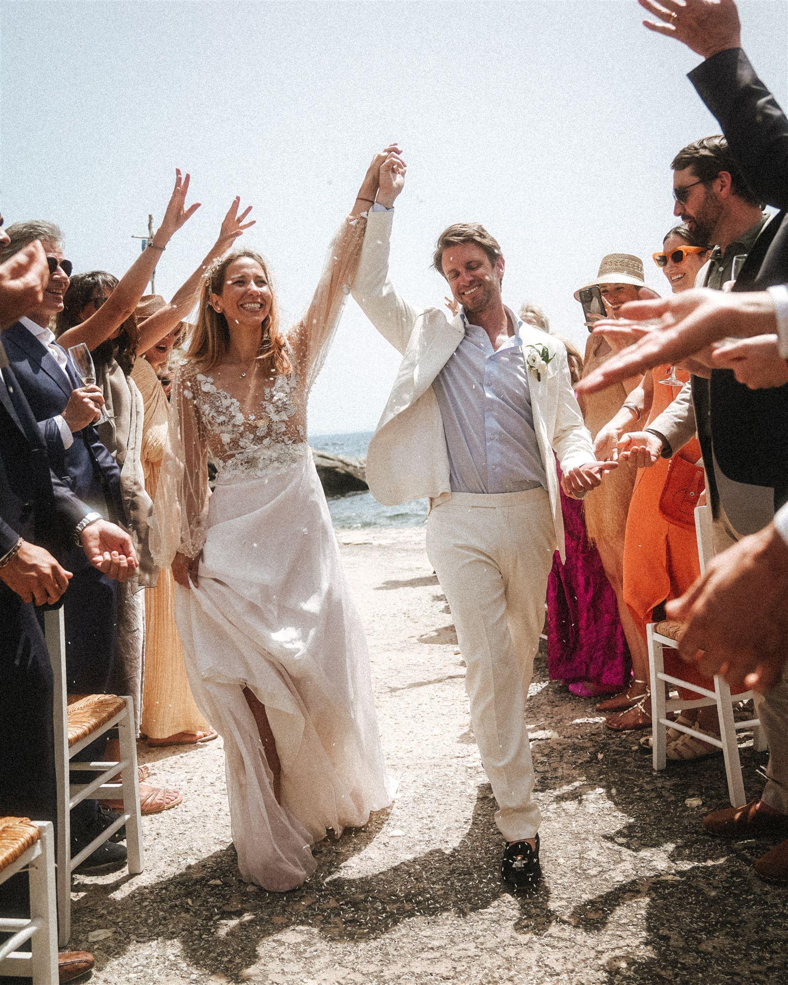 Couple walking back down the aisle after the ceremony, guests raising hands to greet them