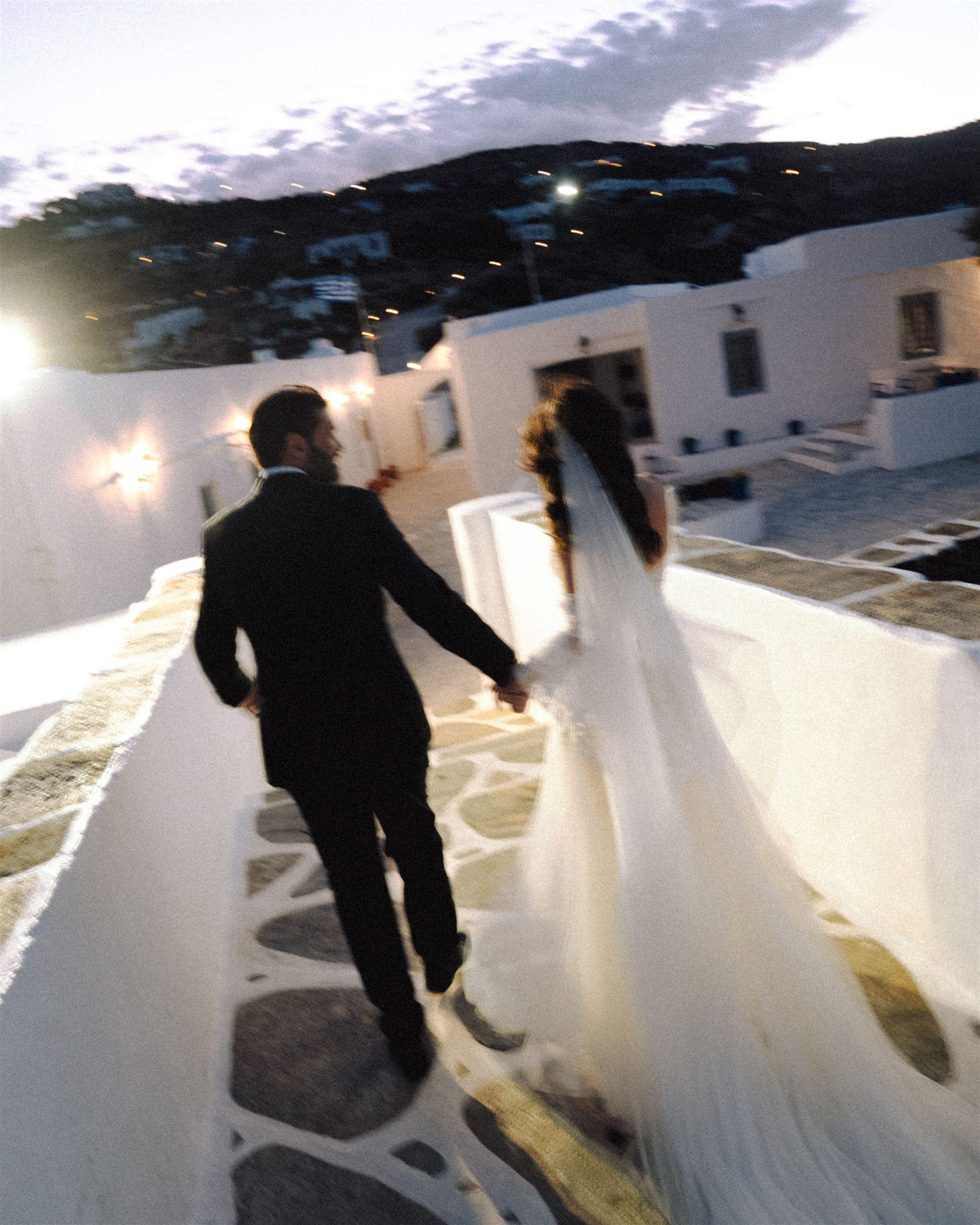 Bride walking away from camera, veil trailing in the wind